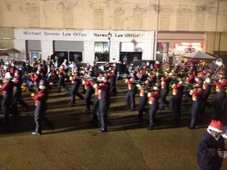 Marching band in red and black uniforms performing on a street at night.
