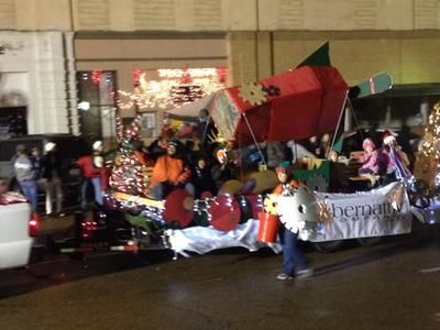Christmas parade float with a red and green structure, people, and lights.