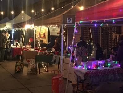 Outdoor market stalls at night, lit by string lights. People browse tables displaying goods.