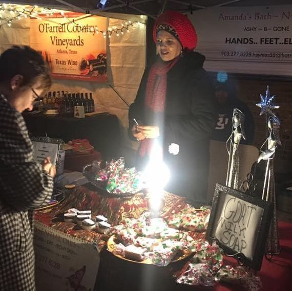 Woman at a craft fair booth selling soaps and pastries. A customer looks at a sign.