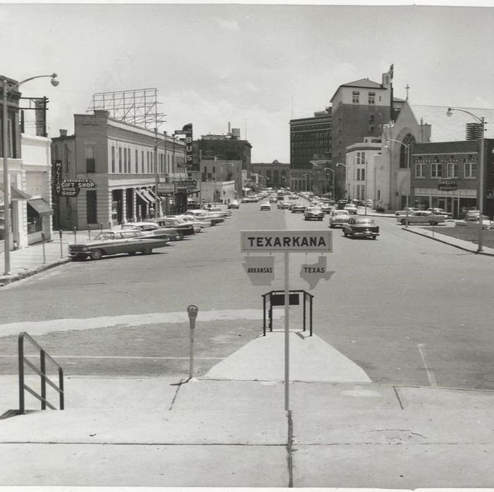Black and white photo of Texarkana street with vintage cars, signs, and buildings.