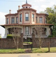 Victorian-style house with brick walls, balcony, and tower. Pink stucco and red tile roof.