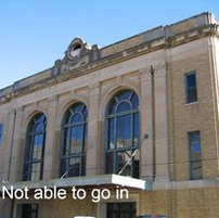 Beige and tan brick building with arched windows and a small balcony under a blue sky.
