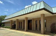 Beige building with a long, angled roof and pillars, under a blue sky.