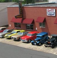 Cars parked in front of Quality Motors, a red brick building with a Kaiser-Frazer sign.