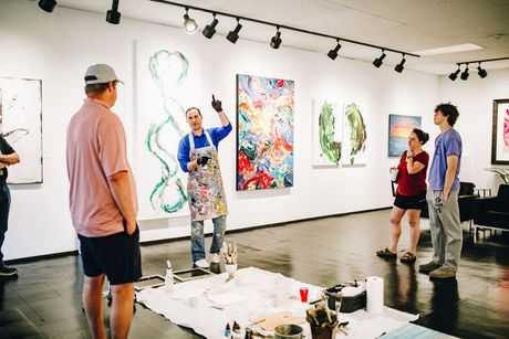 Artist gestures toward artwork, explaining it to a small group in a gallery.