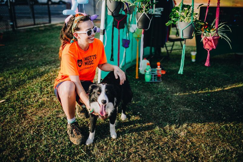 Woman in orange shirt pets a black and white dog outdoors near plants.