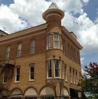 Yellow brick building with a rounded corner turret, arched windows, and a cloudy sky.