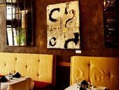 Restaurant interior with yellow booth seating, artwork on brown wall, and mirror.
