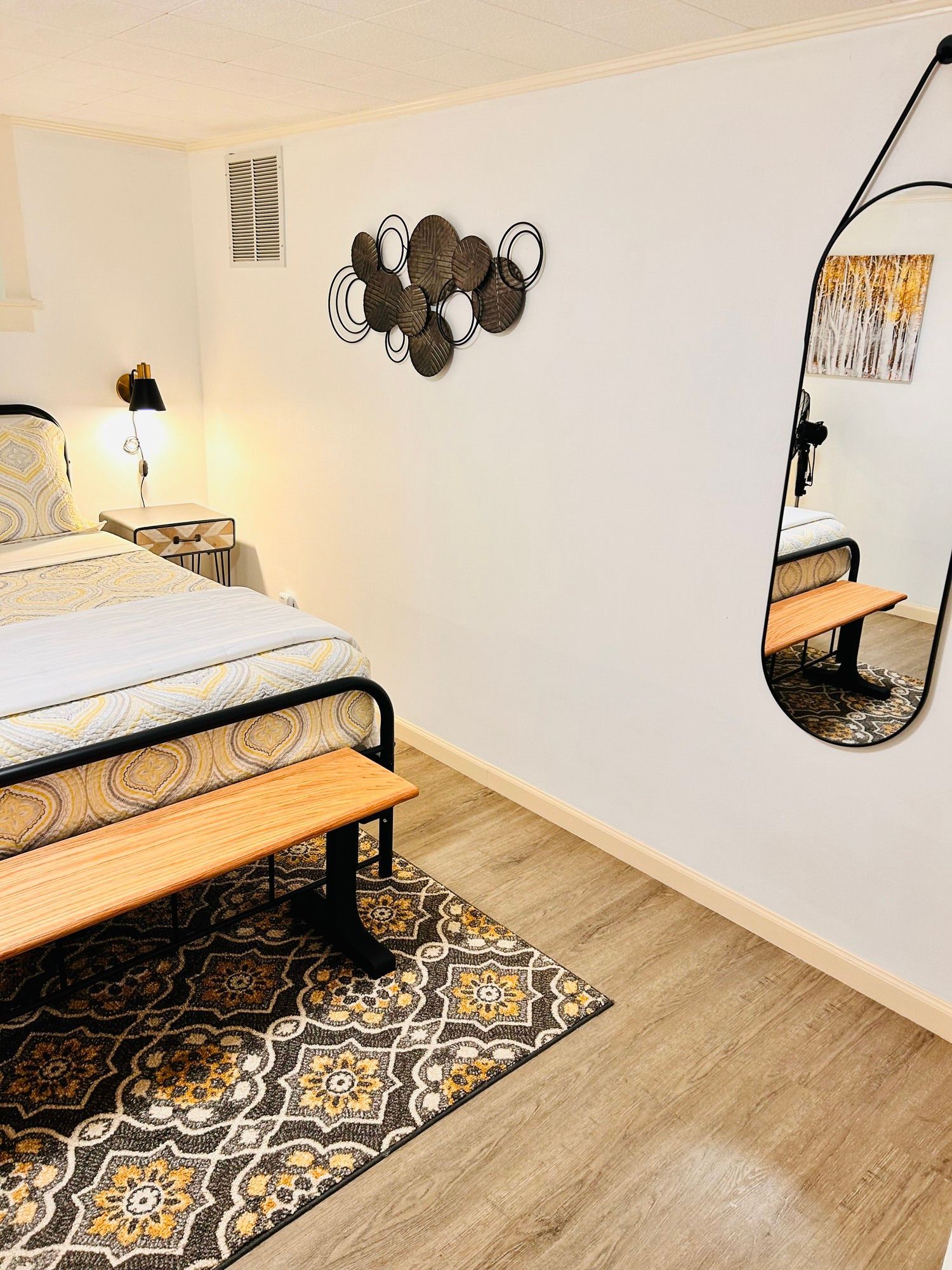 A bedroom with a bed , bench , rug and mirror.