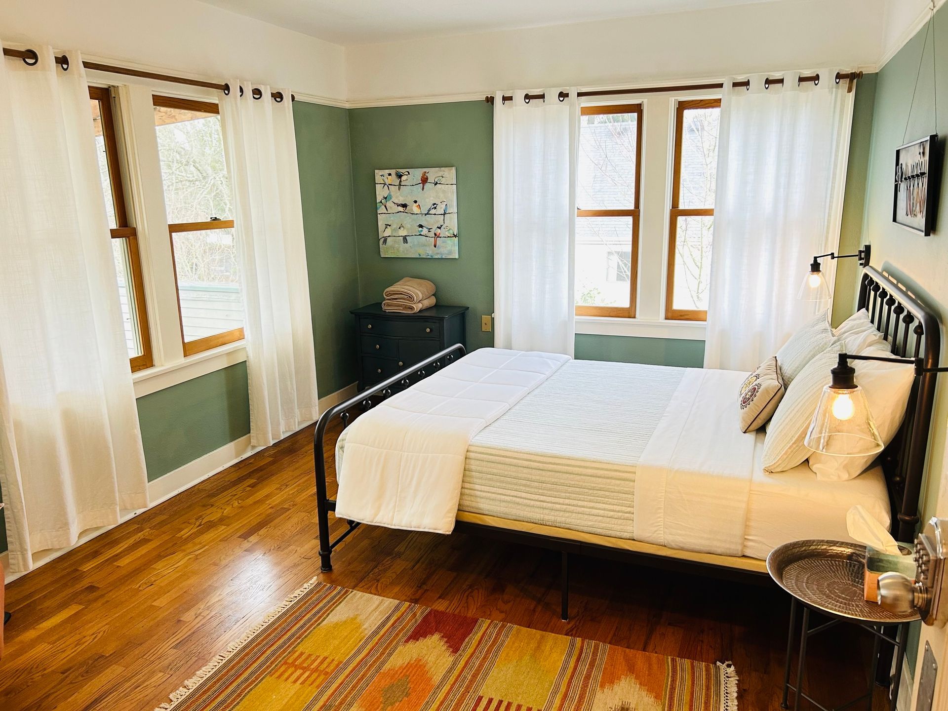 A bedroom with a bed , two windows , a rug and a nightstand.