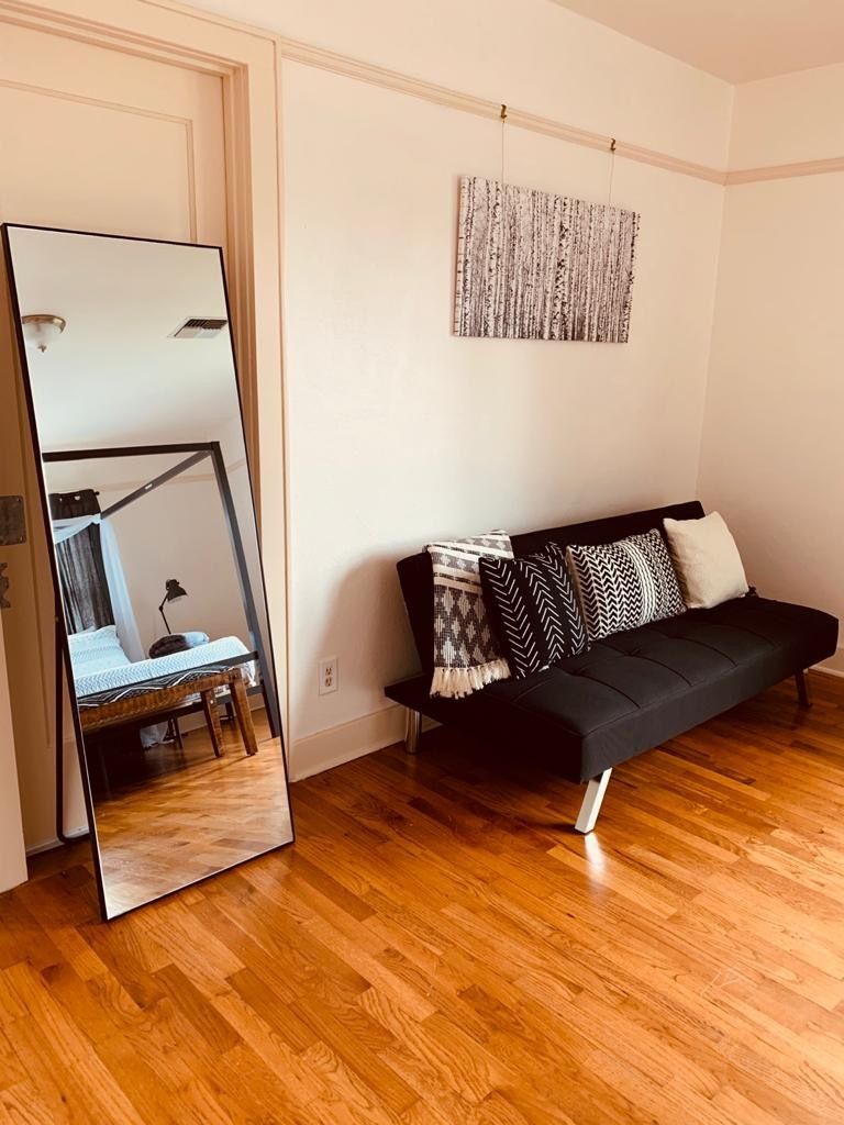 A living room with a black couch and a large mirror.