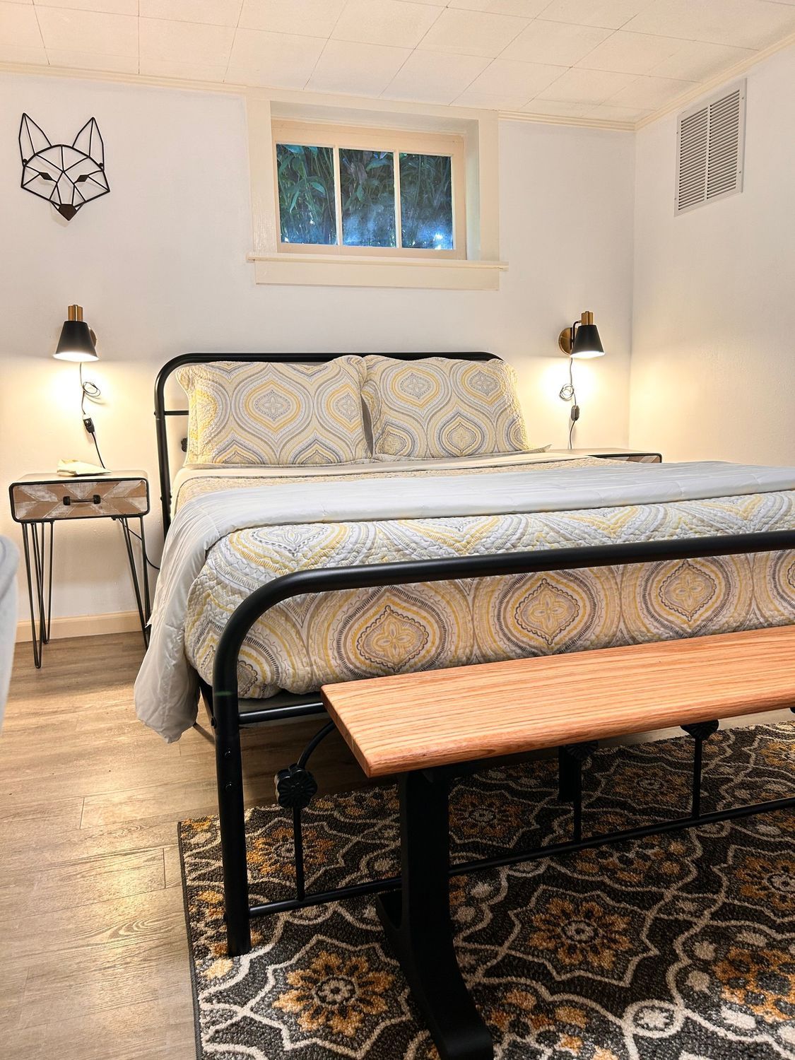 A bedroom with a bed , bench , nightstand and window.