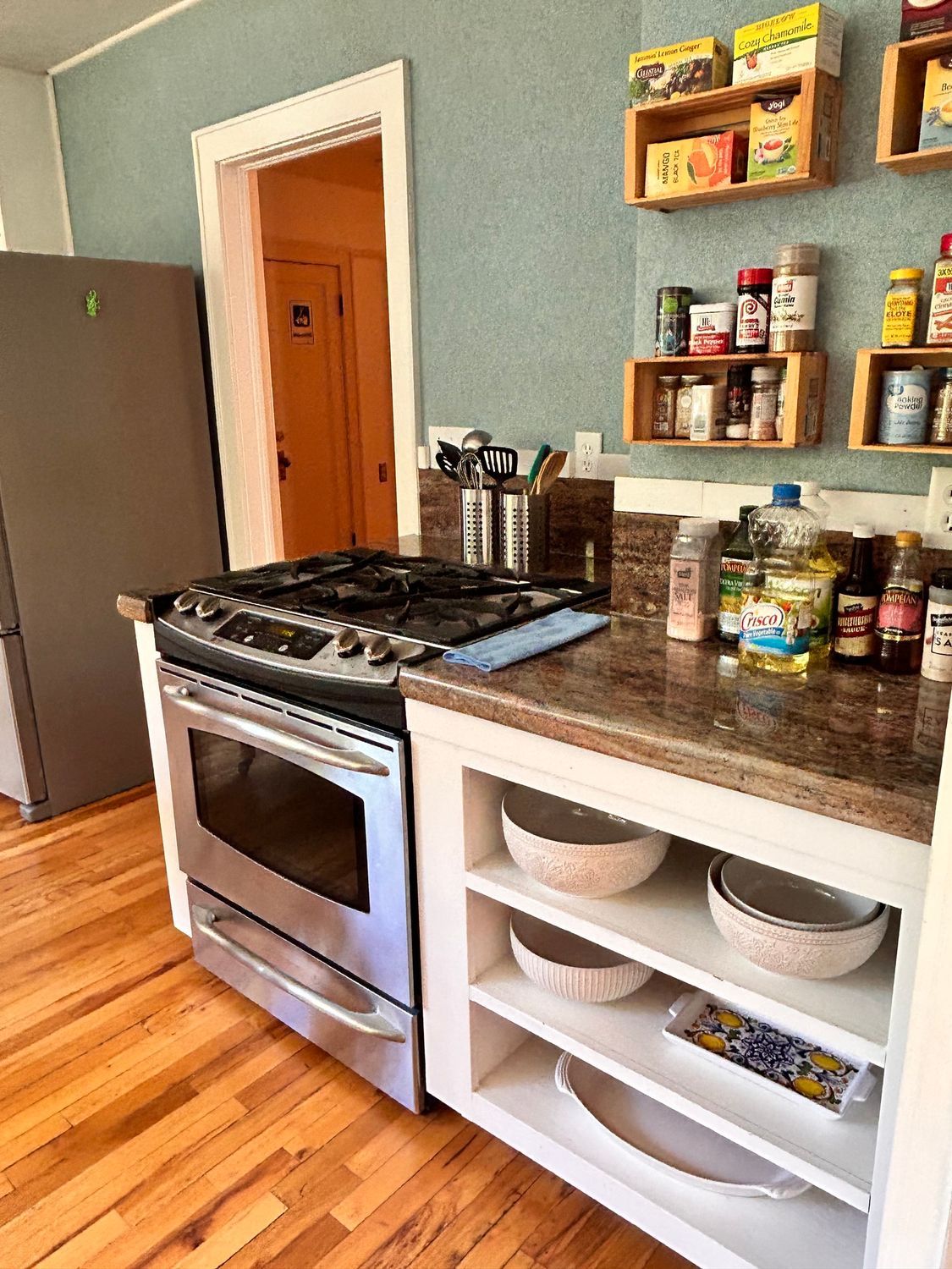 A kitchen with a stove , refrigerator , shelves and bowls on the counter.