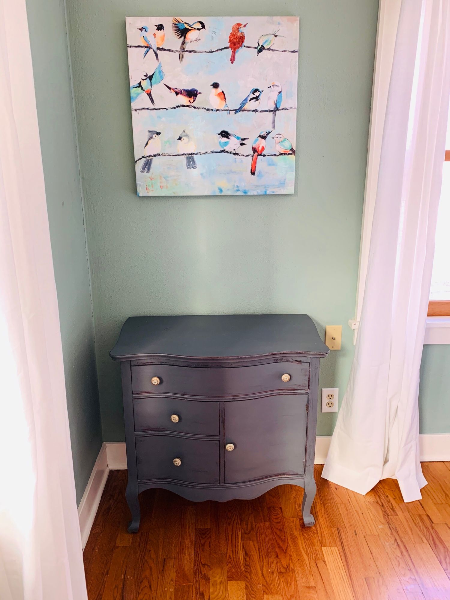 A dresser in a room with a painting of birds on the wall above it.
