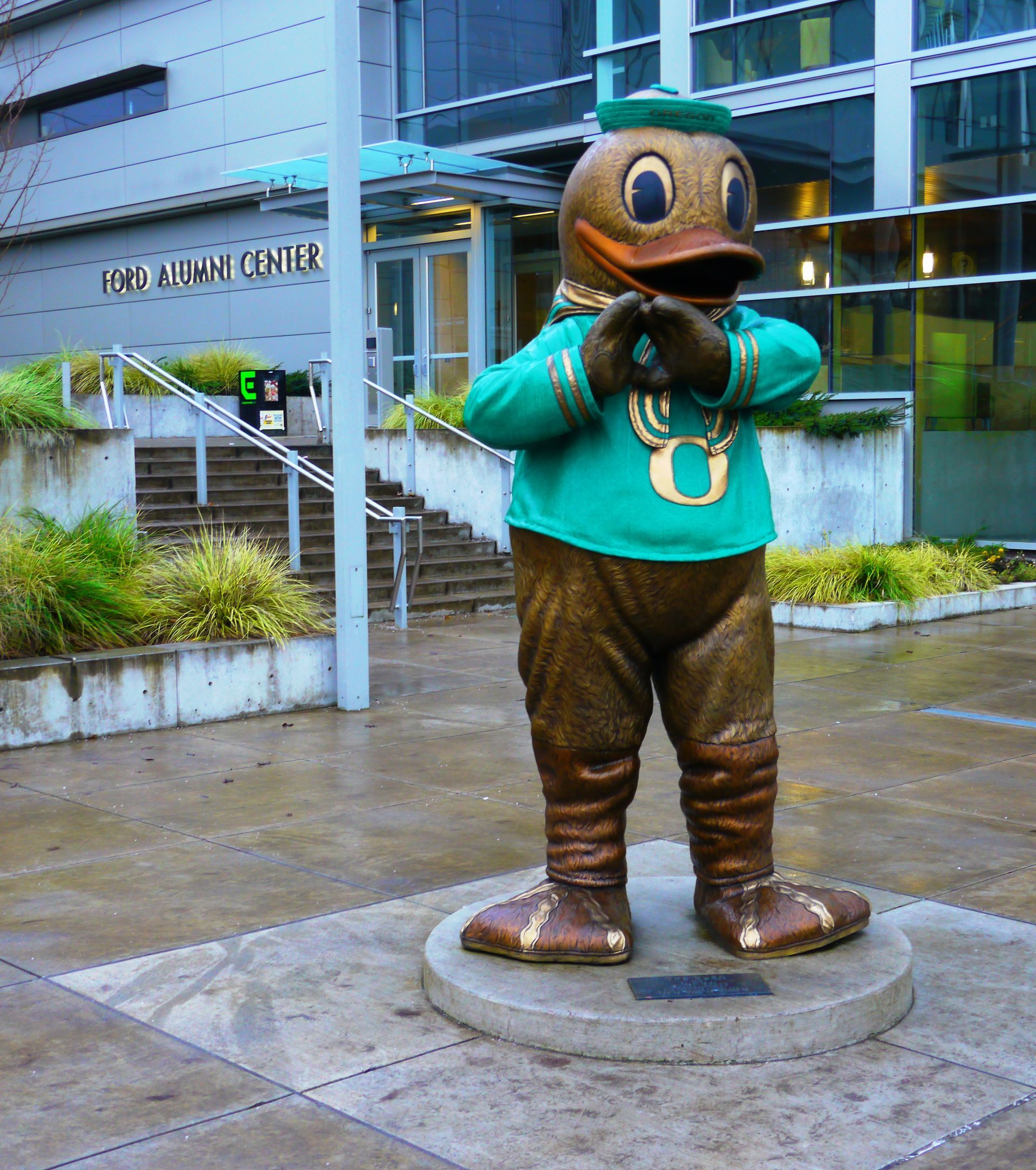 A statue of a duck wearing a green shirt with the letter u on it