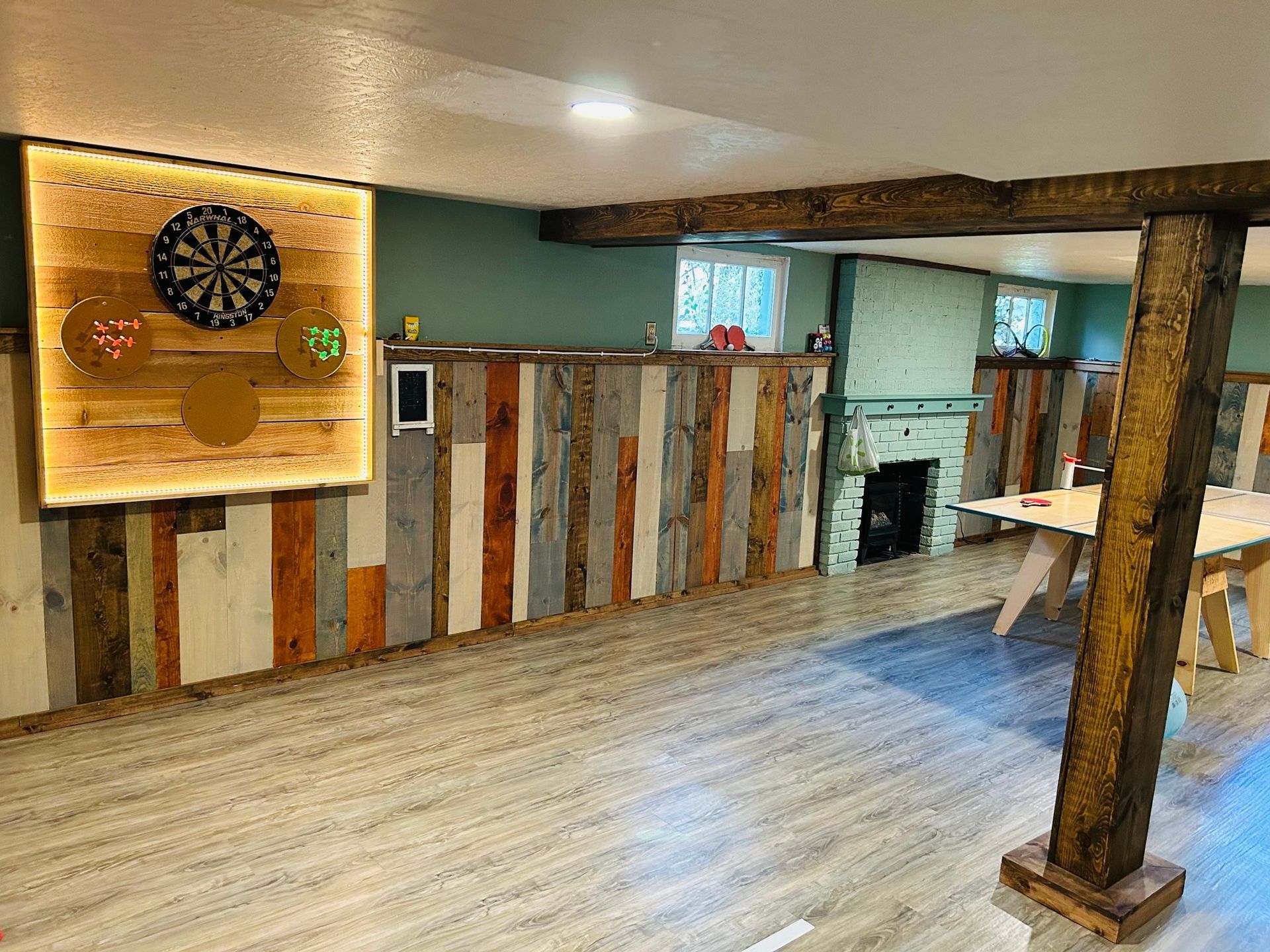A room with a dart board on the wall and a ping pong table.