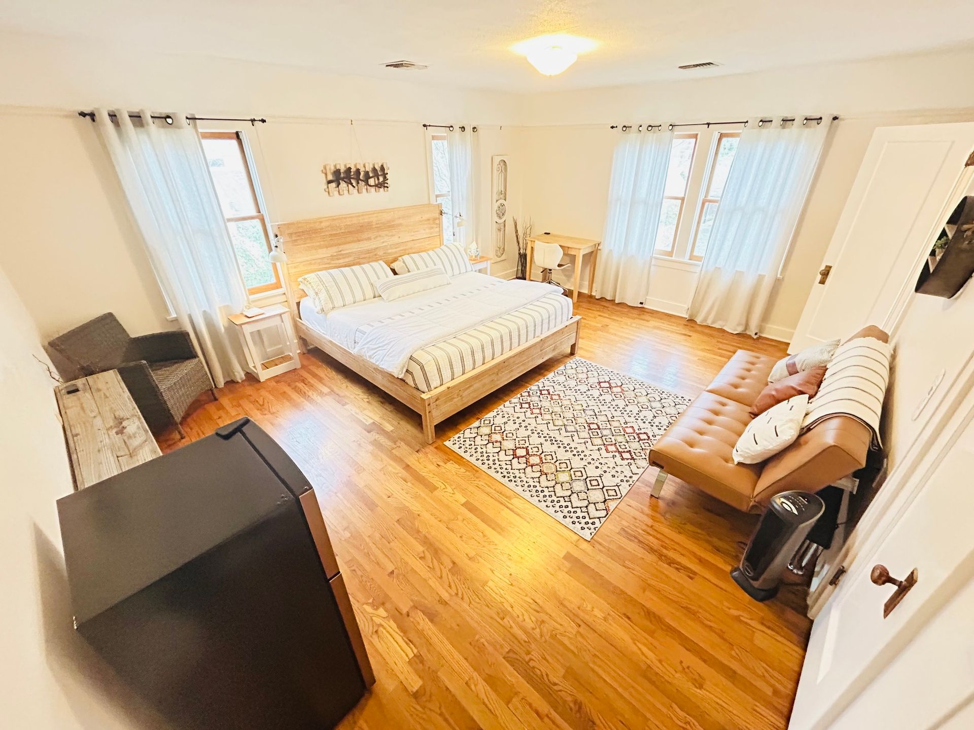 A bedroom with hardwood floors , a king size bed , a couch , and a television.