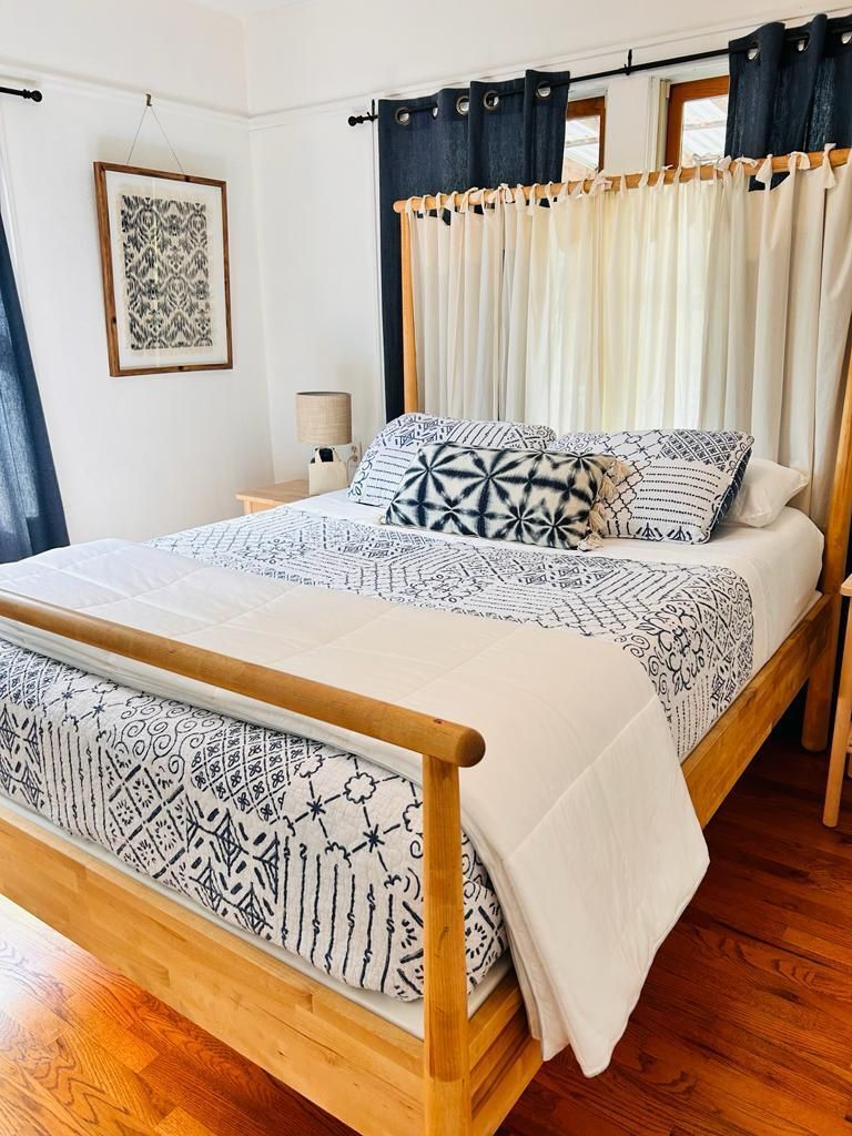 A bedroom with a bed , nightstand , lamp and curtains.