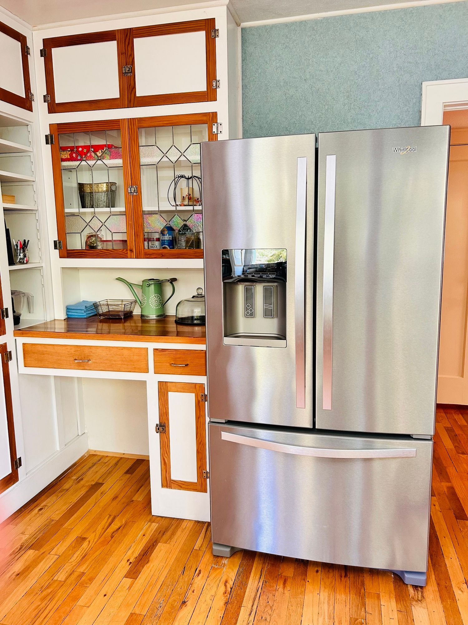A stainless steel refrigerator is sitting on a wooden floor in a kitchen.