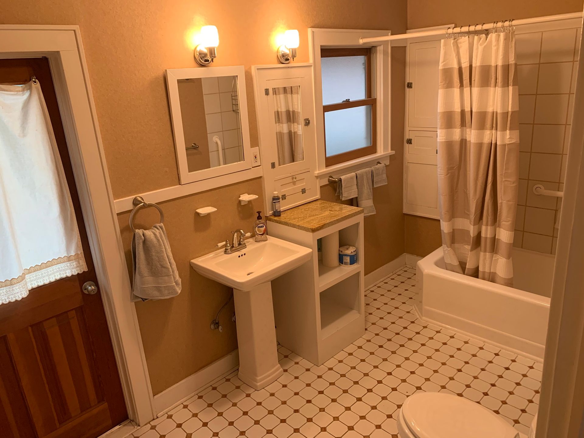 A bathroom with a sink , toilet , shower and window.