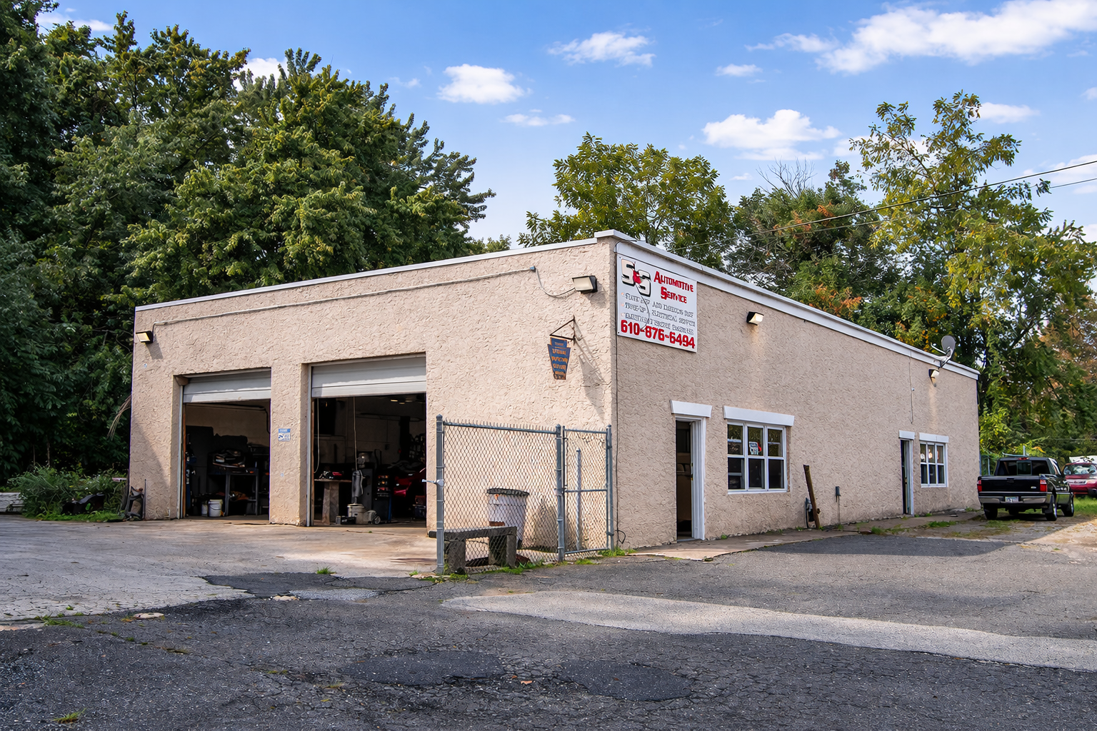 S&S Automotive Service's single-story, beige auto repair shop with two open garage bays, surrounded by trees on a gravel lot.