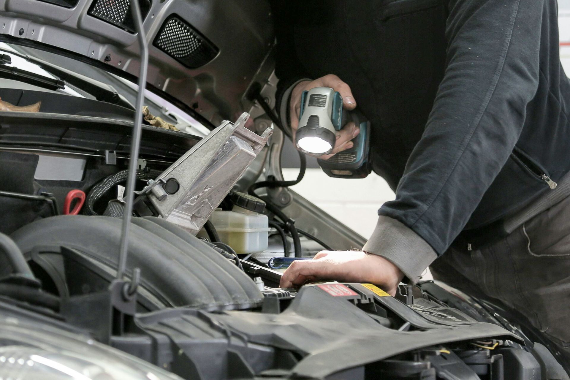 Mechanic from S&S Automotive Service examines car engine with flashlight; workshop setting.