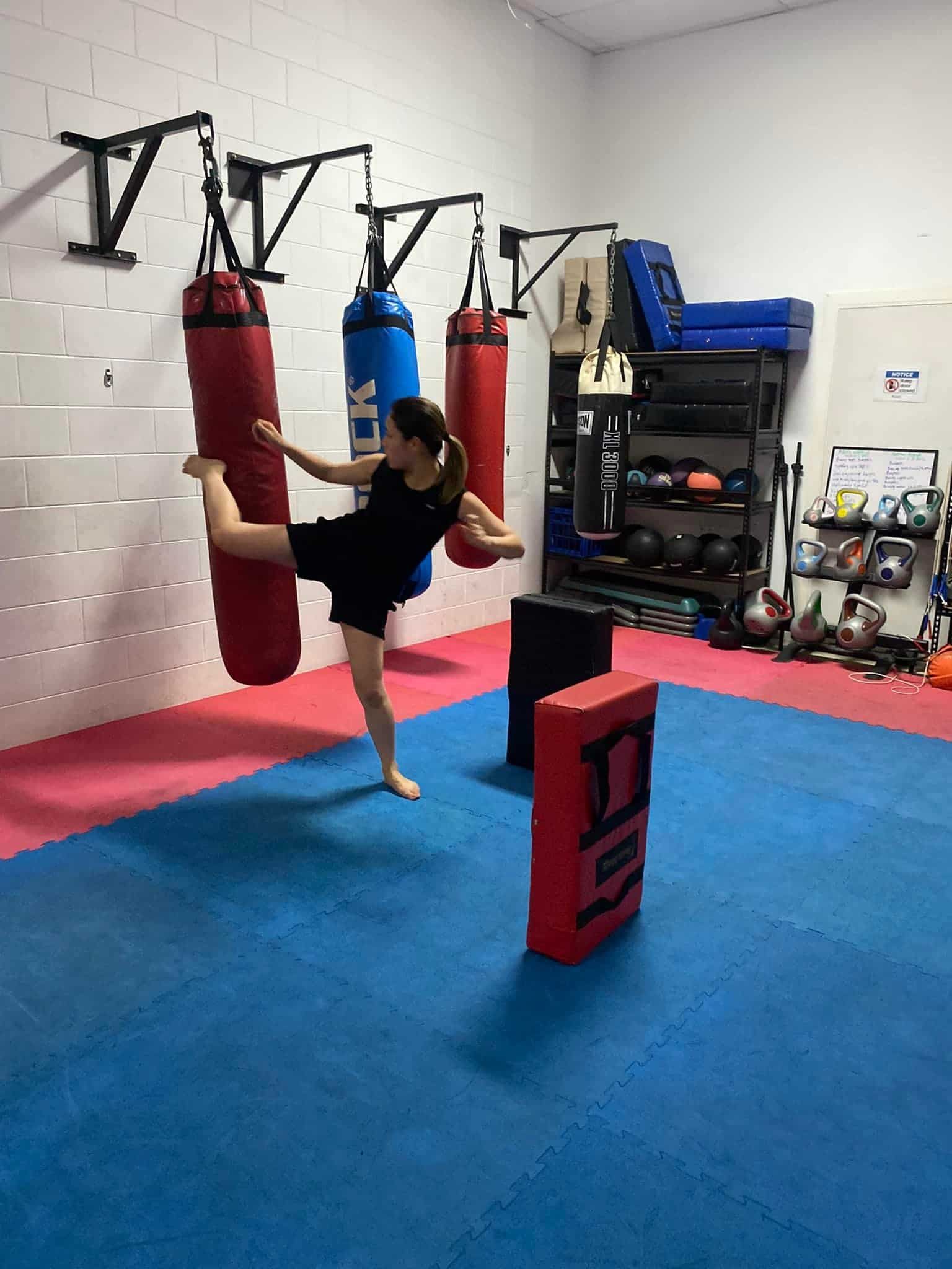 A Girl Attempting To Kick A Boxing Bag During A Training Session — Maxenergy Fitness In Smithfield, QLD