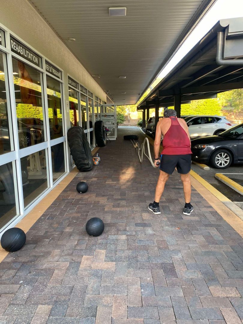 A Man is Holding A Rope In each Hand In A Car Park— Maxenergy Fitness in Smithfield, QLD