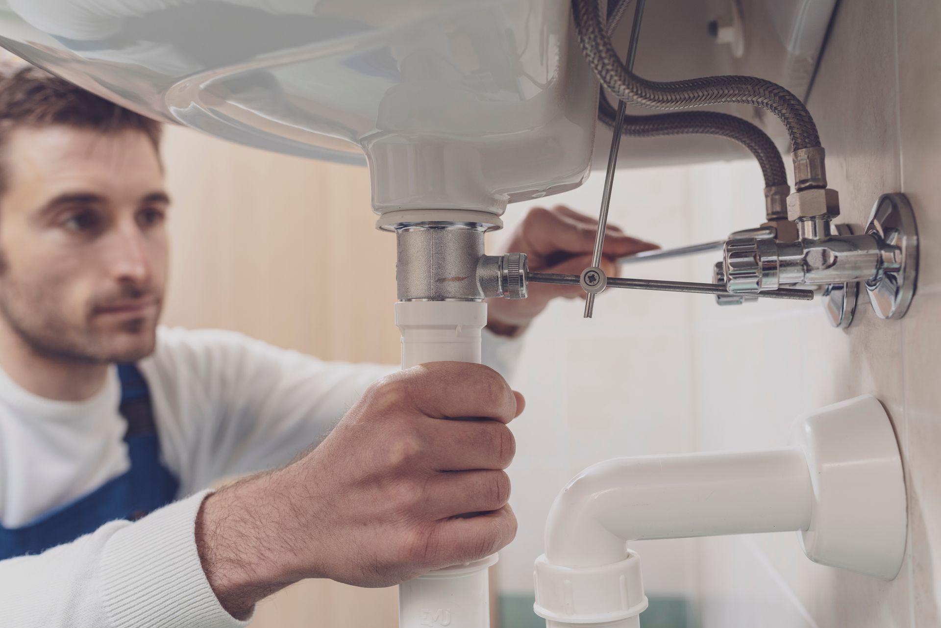 A male plumber tightening sink fittings and pipes during a professional repair service. A male plumber tightening sink fittings and pipes during a professional repair service.