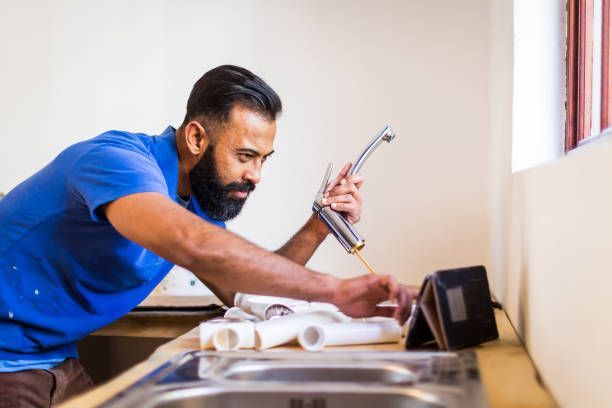 A plumber fitting a tap in the kitchen while using a tablet computer