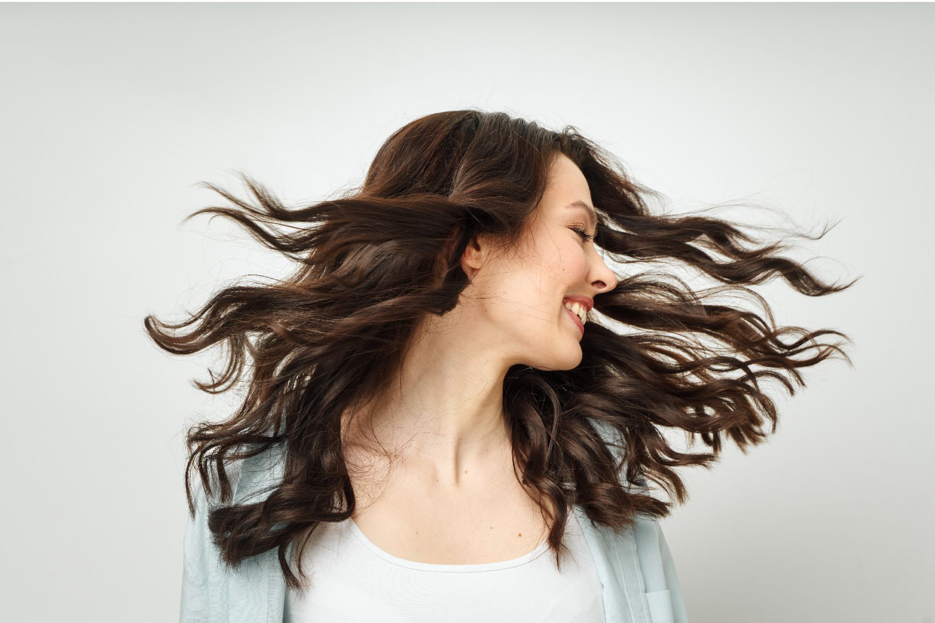 Mujer con cabello oscuro y ondulado, sonriendo, con el cabello volando en el aire, sobre un fondo blanco.