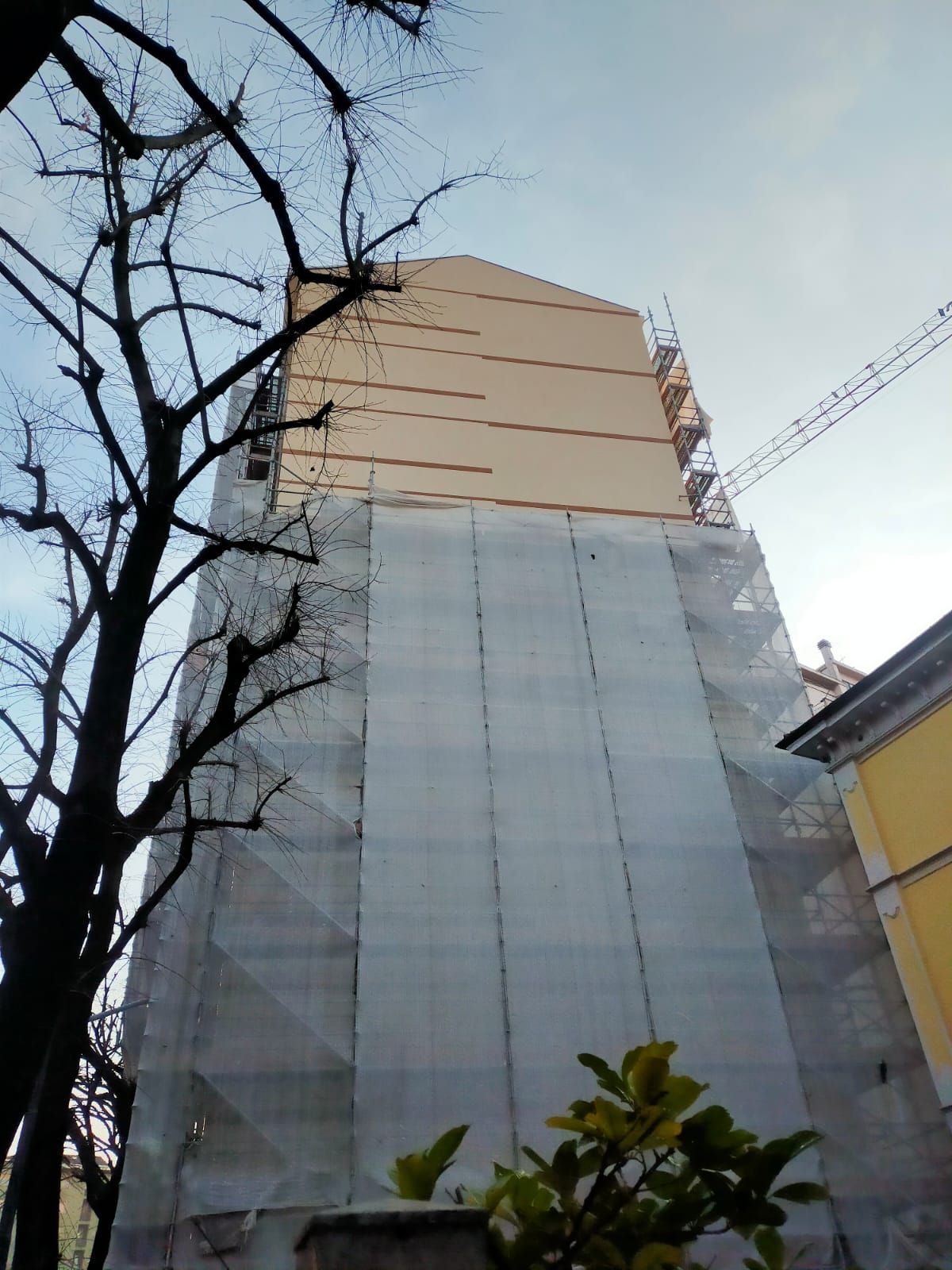 un edificio alto con impalcature attorno e una gru sullo sfondo