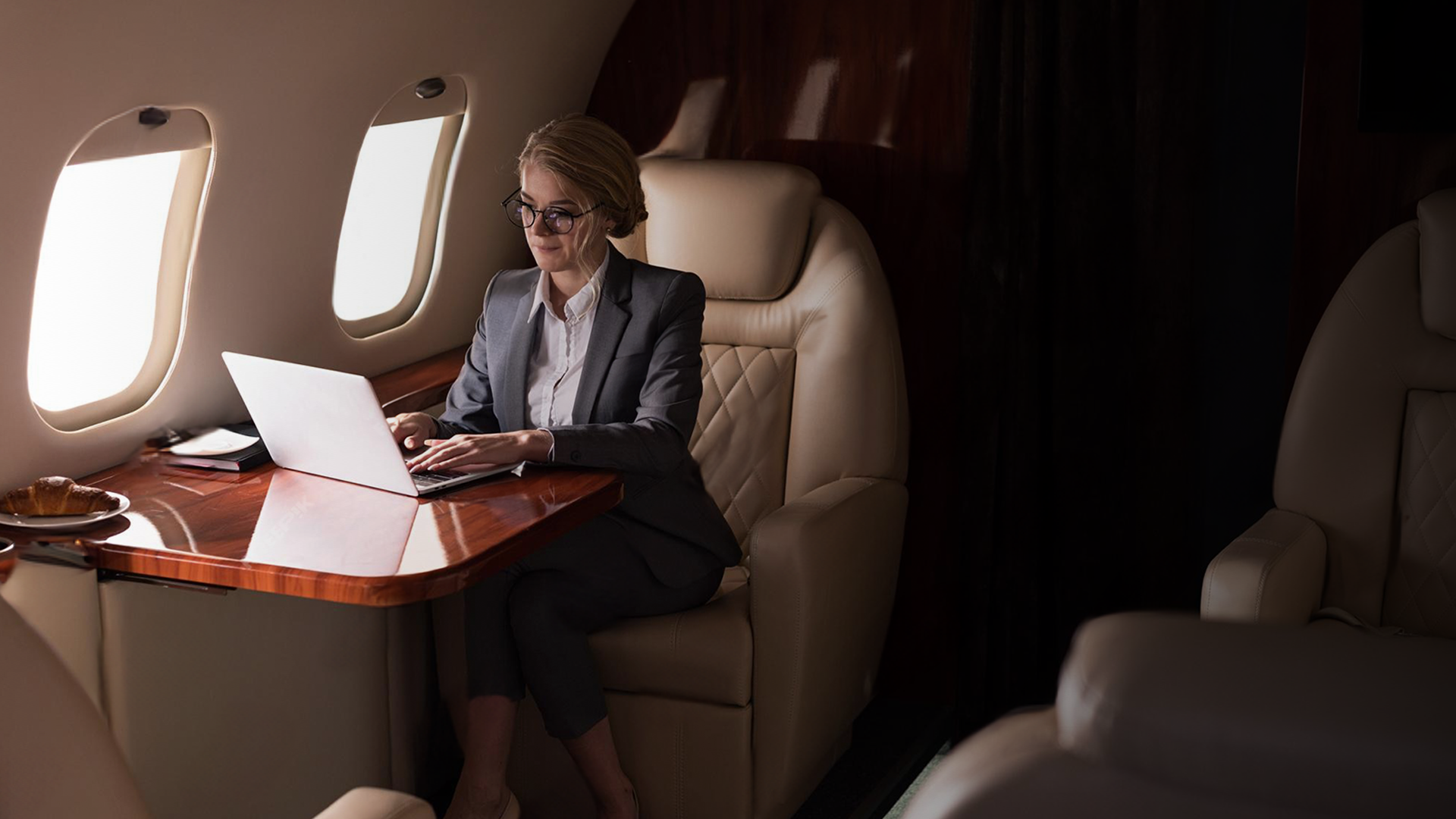 A woman is sitting at a table on an airplane using a laptop computer.
