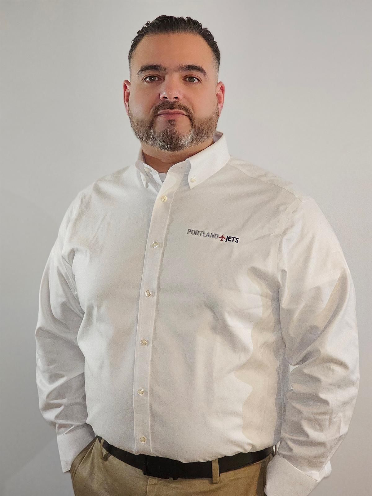 A man with a beard is wearing a white shirt and khaki pants.