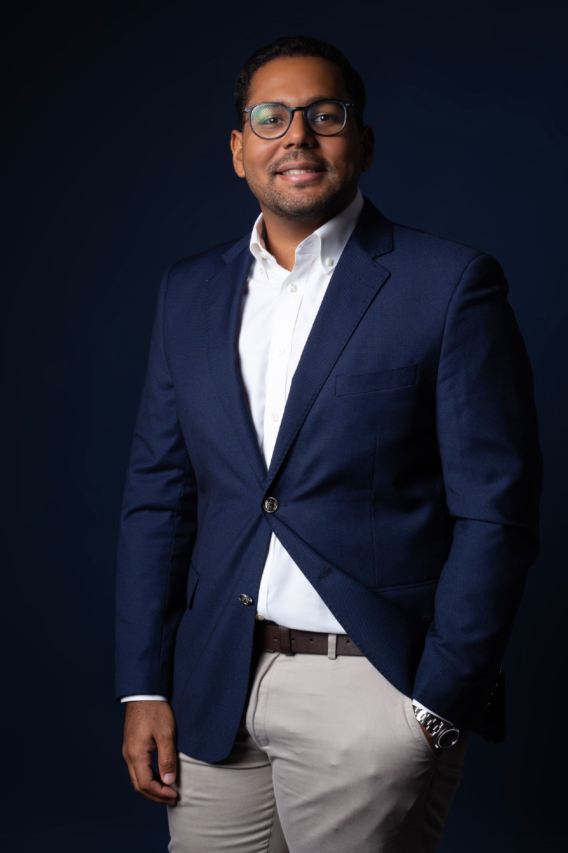 A man in a blue jacket and white shirt is standing with his hands in his pockets.
