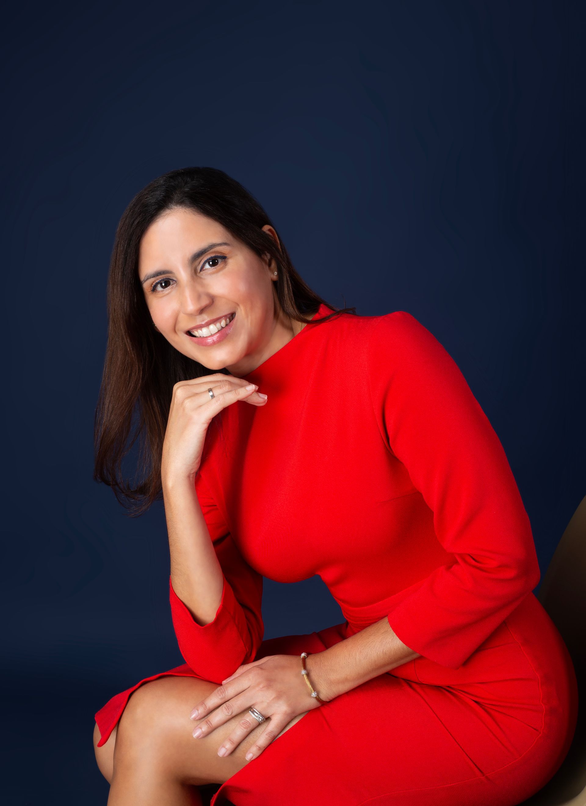A woman in a red dress is sitting on a chair and smiling.