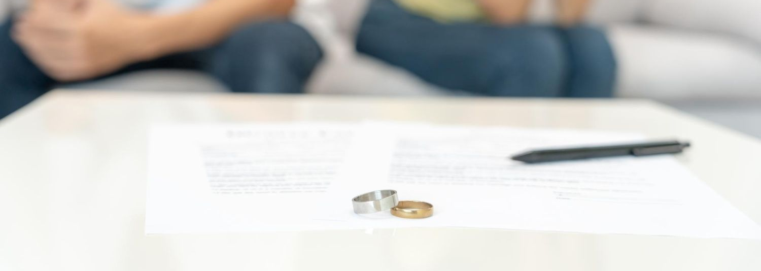 Wedding rings on a divorce paper, with blurred people on a couch.