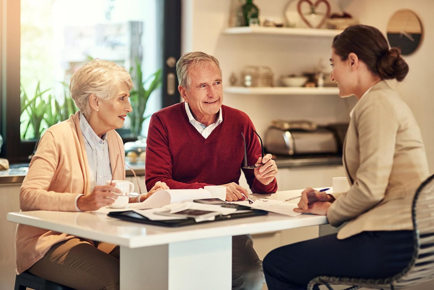 Older couple in a kitchen meeting with a financial advisor. Discussing paperwork at a table.