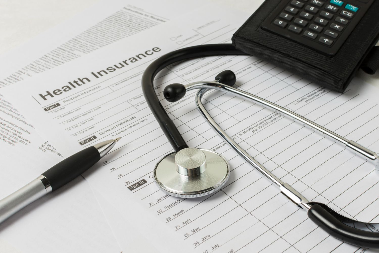 Health insurance form, stethoscope, calculator, and pen on a desk, representing healthcare costs.