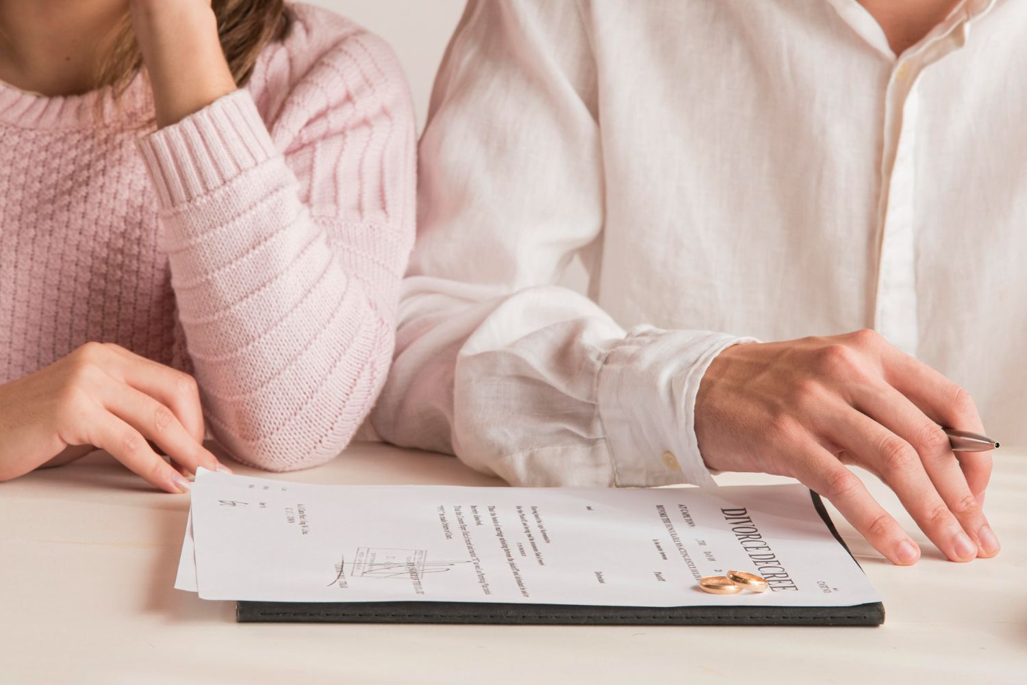 Couple at table with divorce papers; woman sad, man holding pen.