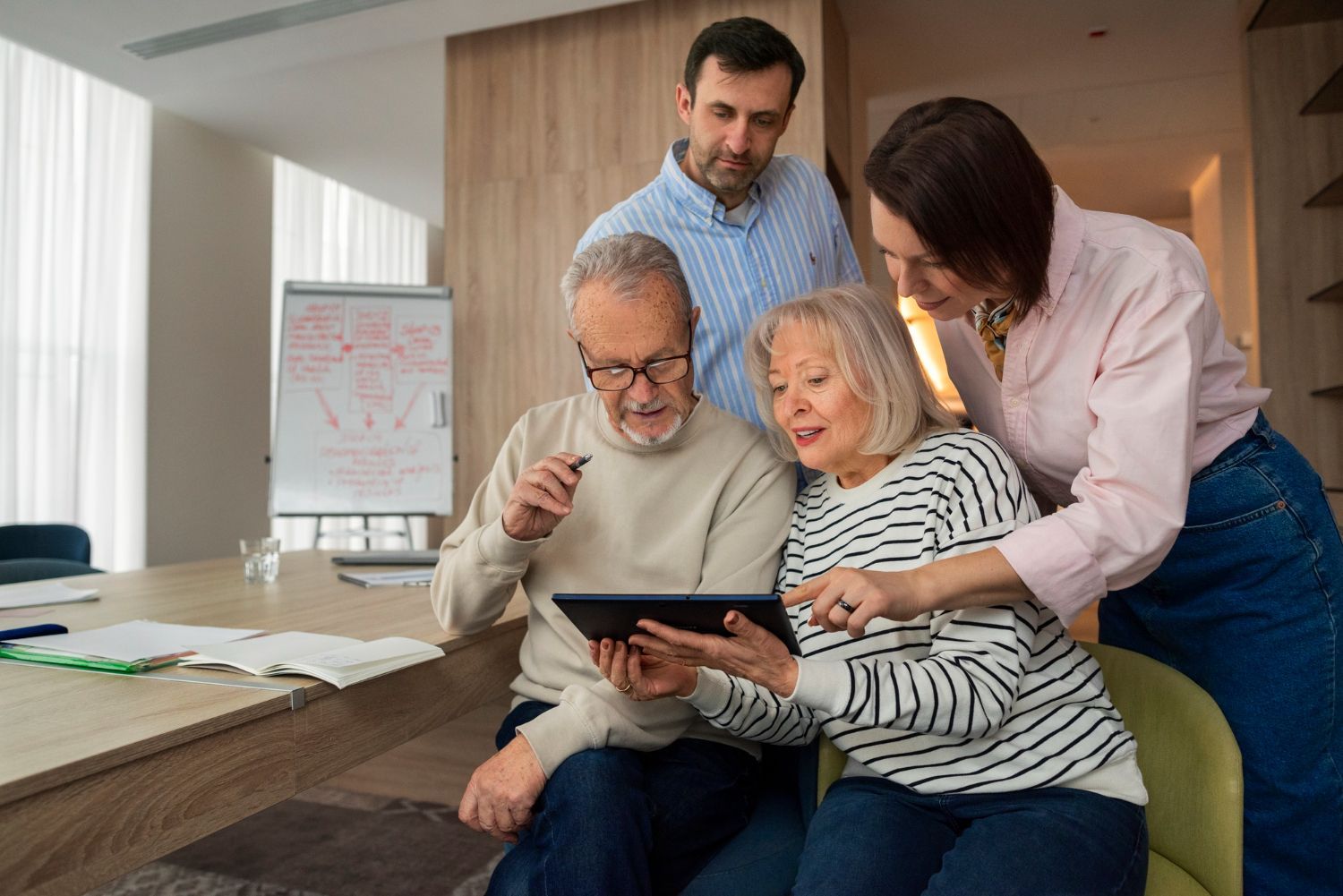 Four people, including two older adults, looking at a tablet together in a meeting room.