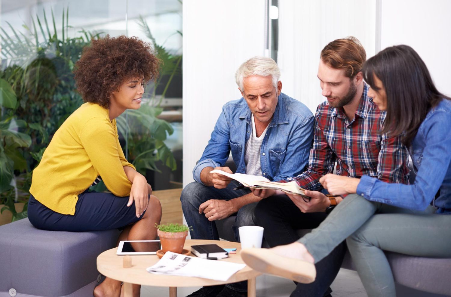 Four people in a collaborative meeting: examining papers together, smiling, indoors.