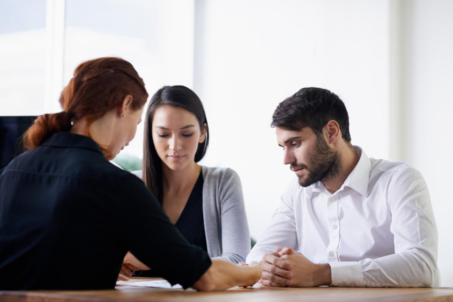 A woman in black jacket reviews paperwork with a couple seated at a table.