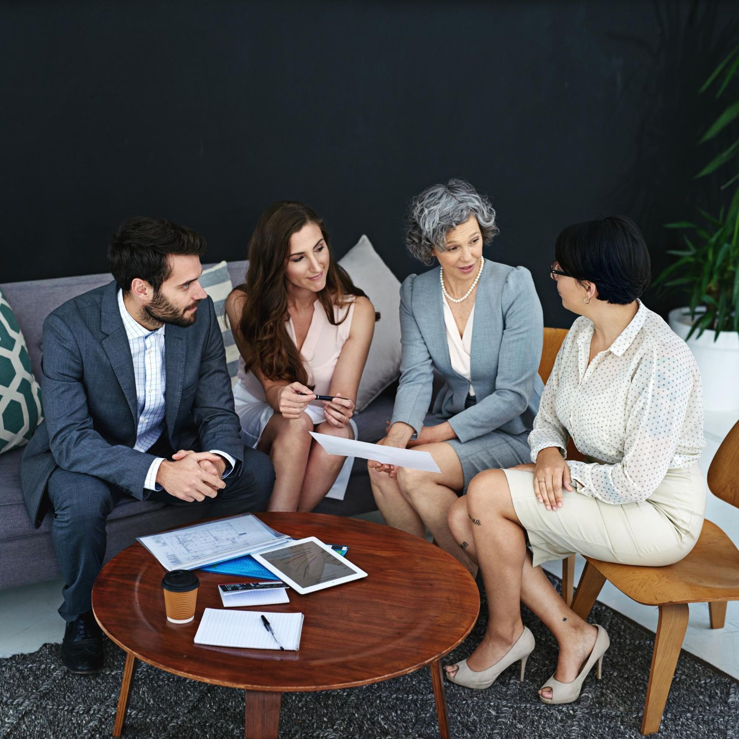 Four businesspeople in a meeting, discussing documents. They sit in a modern office space.