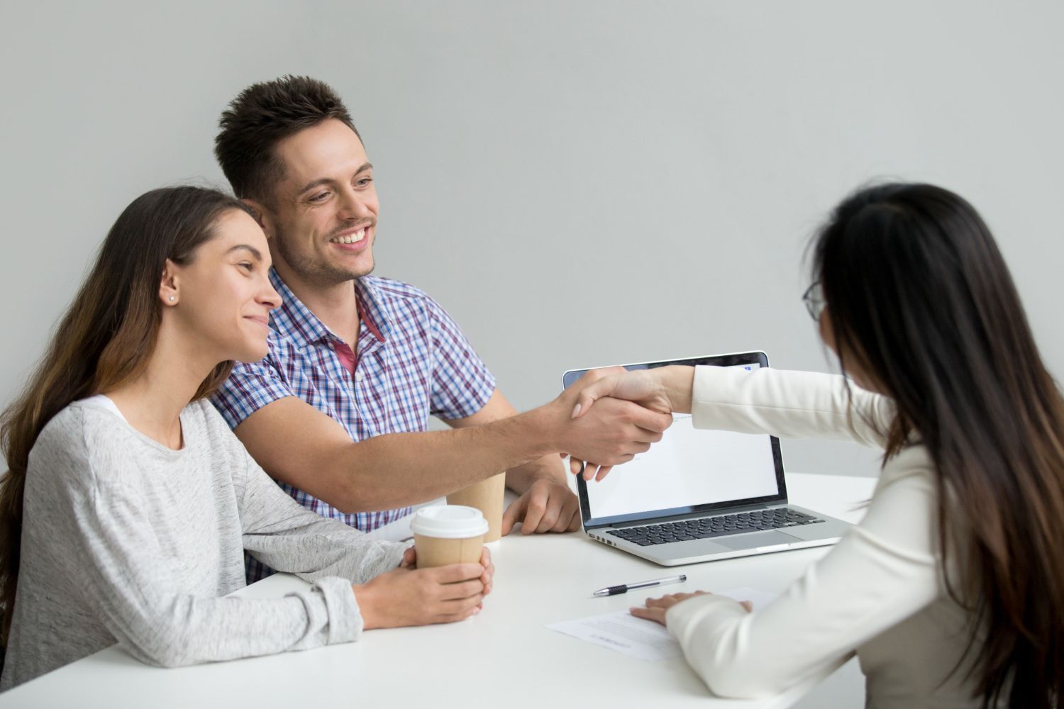 Couple shaking hands with a person at a table, possibly finalizing a deal.