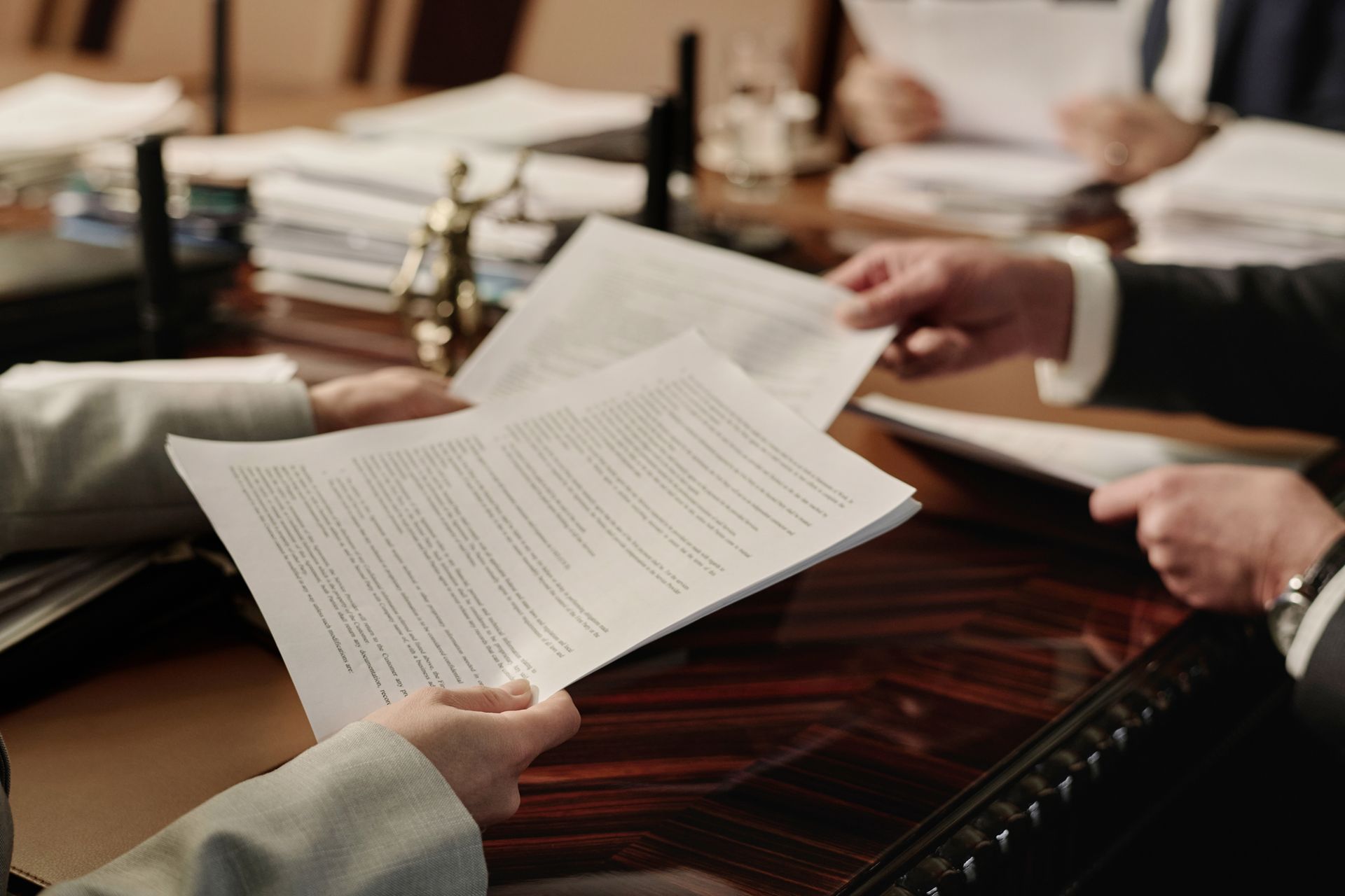 Hands holding and passing papers across a dark wooden table, in a professional setting.