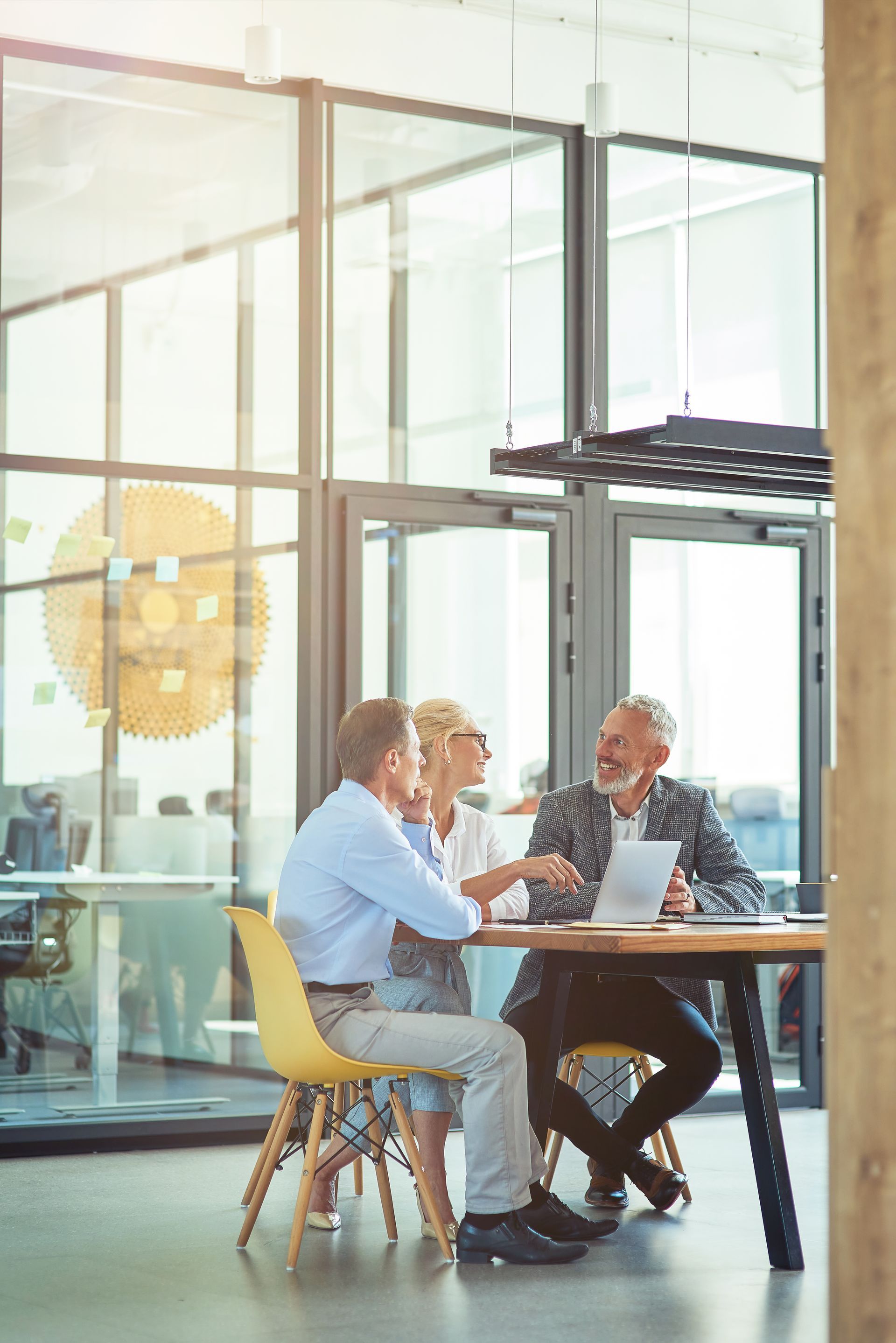 Three professionals in business attire at a table, discussing a tablet in a modern office setting.