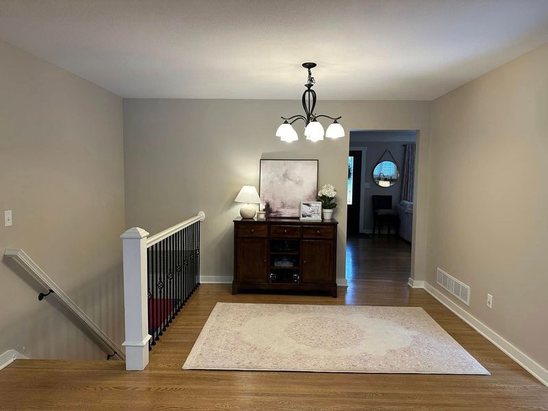 A living room with hardwood floors , a rug , a dresser and a chandelier.