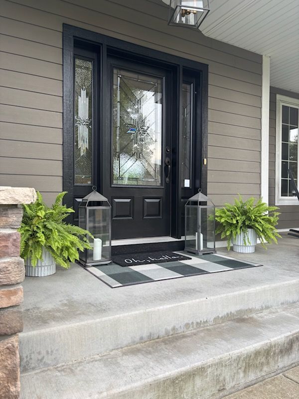 A black front door with a stained glass window is on a porch.
